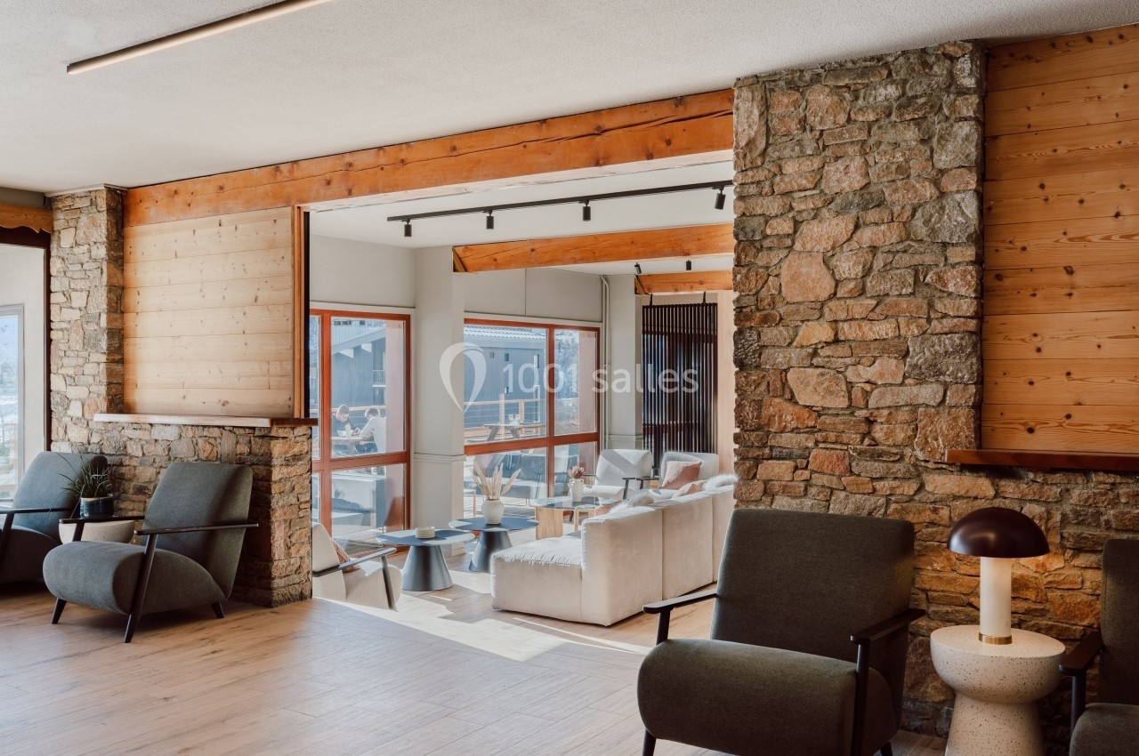 Espace intérieur lumineux avec murs en pierre, fauteuils modernes et vue sur une terrasse extérieure.