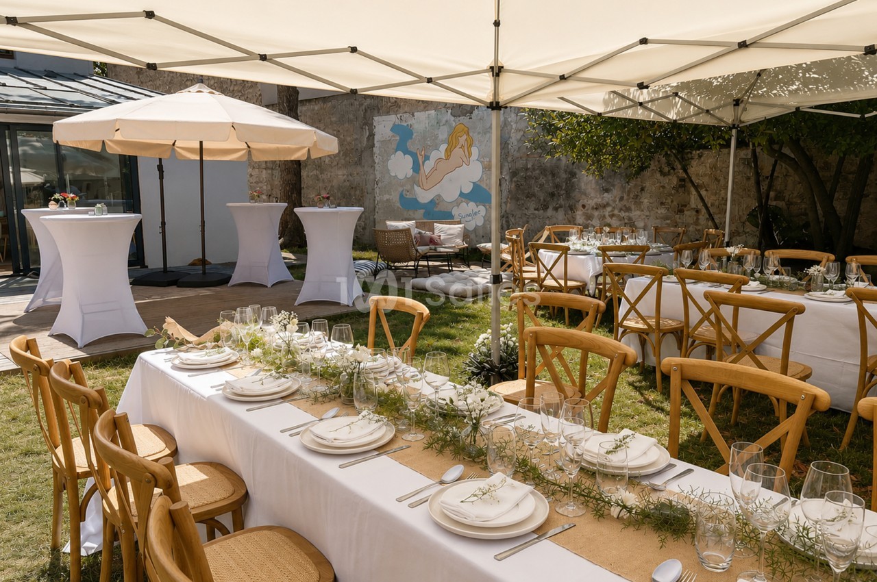 Terrasse dressée sous tentes avec tables blanches, chaises bois, couverts et verres - mur ancien avec fresque bleue en arrière-plan.
