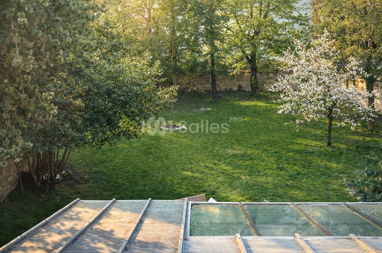 Jardin arborisé avec pelouse, arbres en fleurs blanches et structures de terrasse en bois au premier plan.