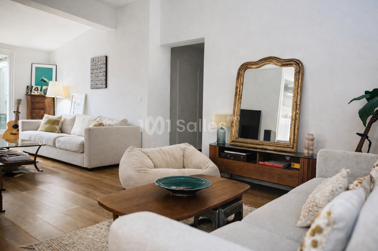 Salon spacieux aux murs blancs avec canapés beige, table basse en bois et miroir doré.