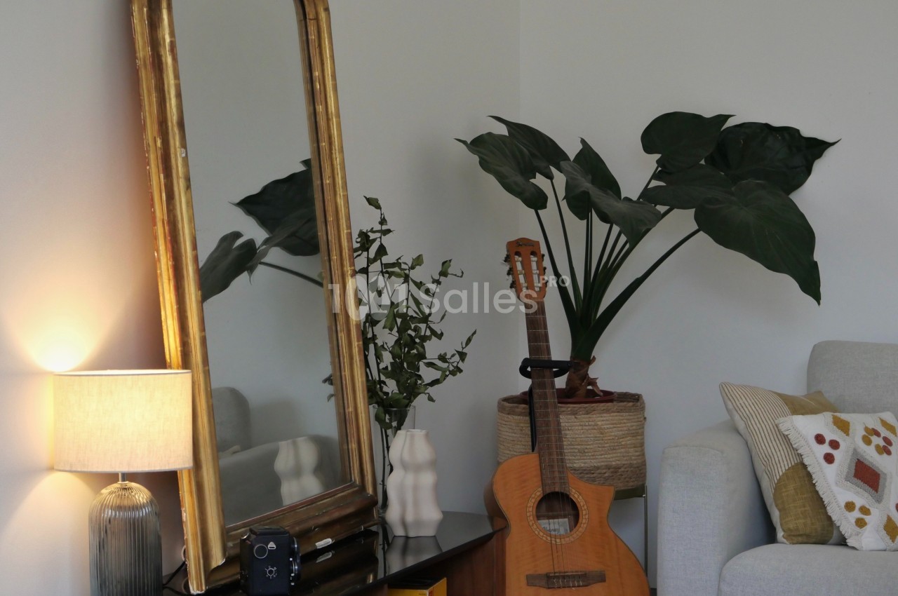 Miroir encadré de doré, lampe allumée, guitare acoustique et plantes vertes en pots sur meuble.