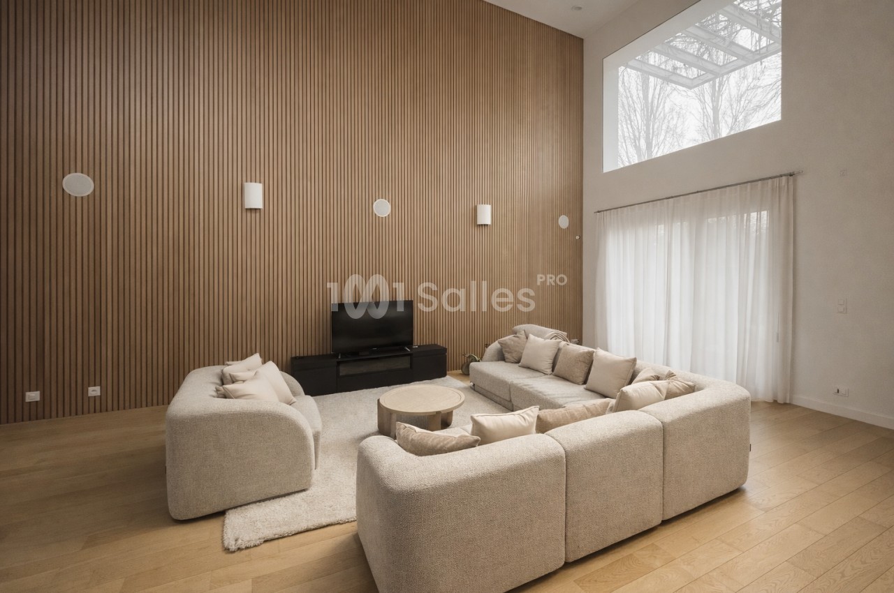 Salon spacieux avec canapés modulaires beige, mur à lamelles bois et baies vitrées apportant la lumière naturelle.