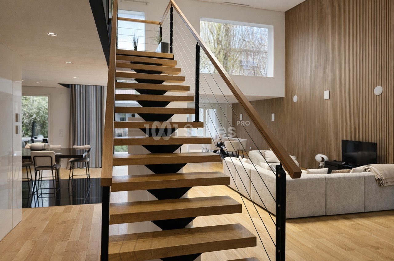 Escalier en bois avec rampe métallique reliant deux étages d'un intérieur moderne et lumineux.