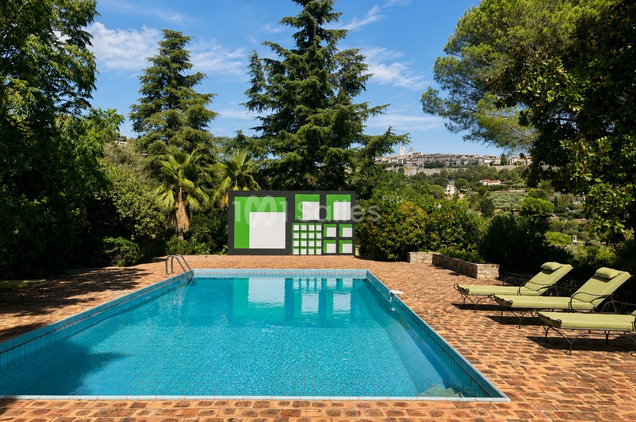 Piscine rectangulaire entourée de chaises longues, terrasse en brique, végétation dense et vue sur un village en arrière-plan.