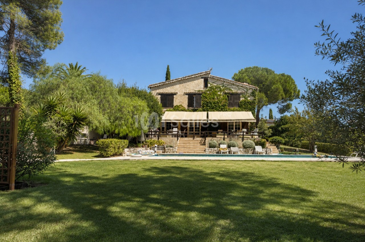 Villa provençale avec piscine, terrasse ombragée et jardin paysager, sous ciel dégagé.