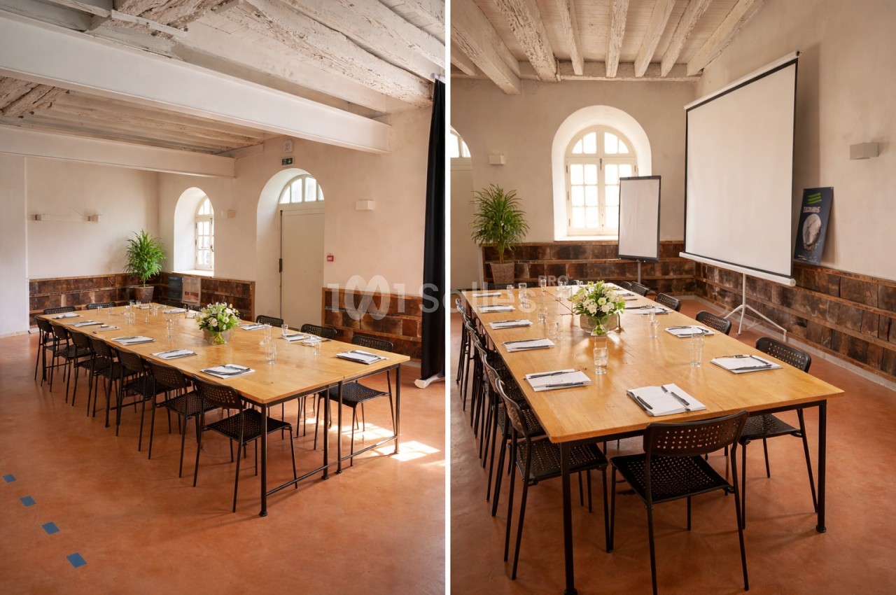 Salle de réunion lumineuse avec tables en bois disposées en rectangle, chaises noires, écran de projection et plantes…