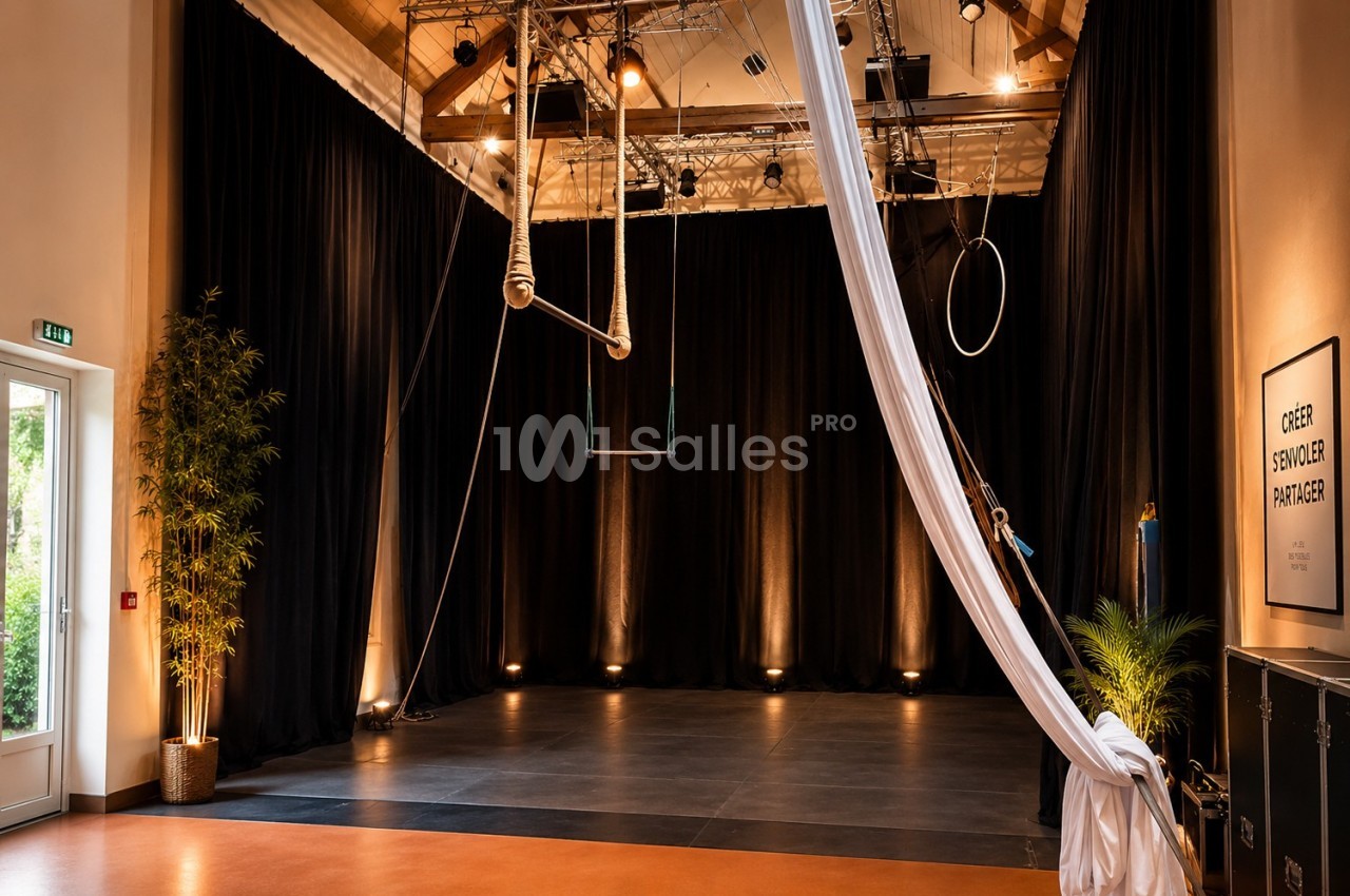 Salle de spectacle avec scène vide, rideaux noirs, équipements aériens suspendus et éclairage tamisé.