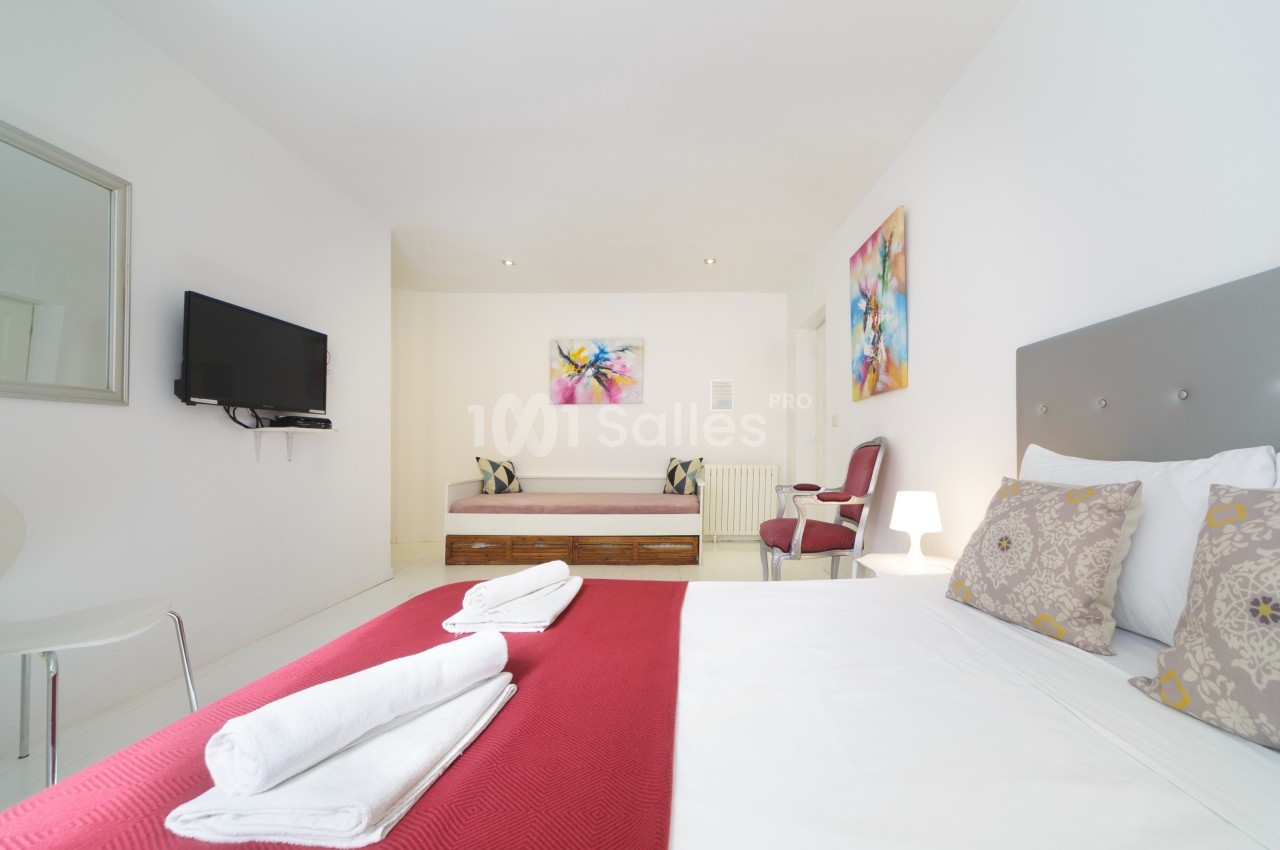 Chambre lumineuse avec lit double, canapé, télévision murale et décorations colorées sur les murs.