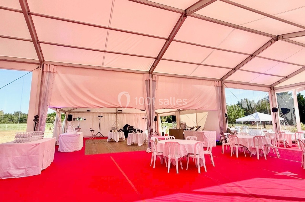 Intérieur d'une tente événementielle avec sol rouge, tables et chaises blanches, et espaces aménagés pour un buffet.