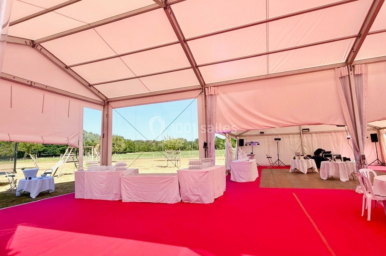 Intérieur d'une tente événementielle avec sol rose, tables blanches et vue sur un espace extérieur verdoyant.