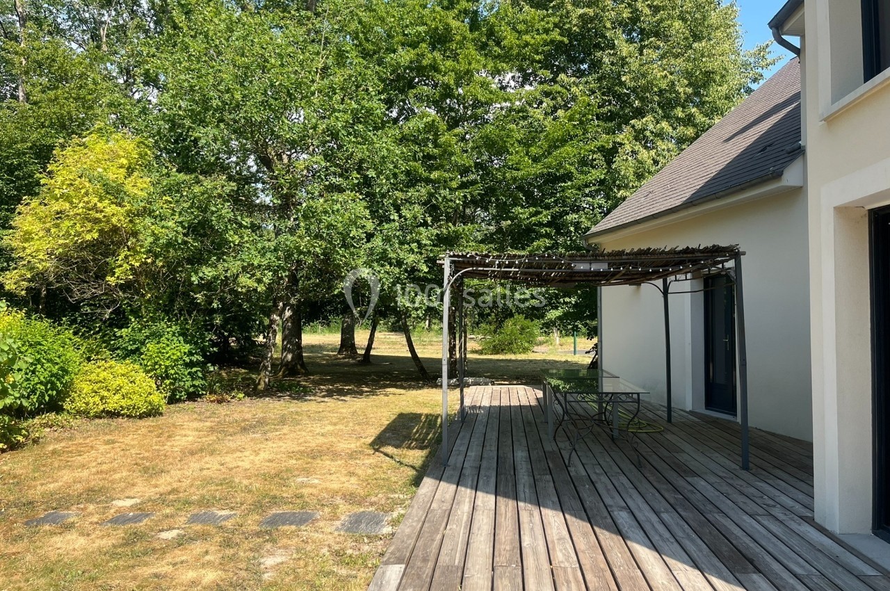 Terrasse en bois avec pergola ombragée, donnant sur un jardin arboré par une journée ensoleillée.