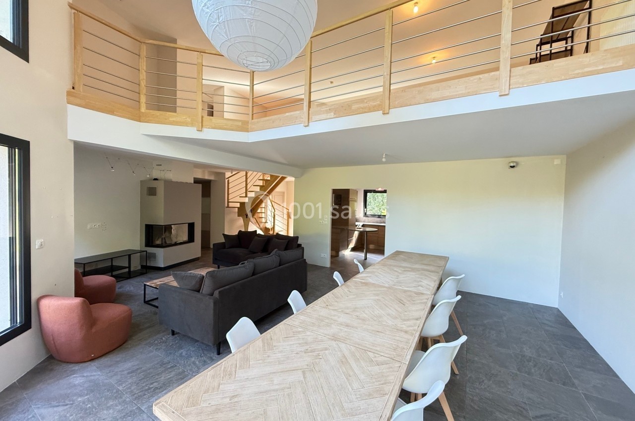 Salle à manger spacieuse avec une grande table en bois, salon avec canapé et mezzanine visible au plafond.