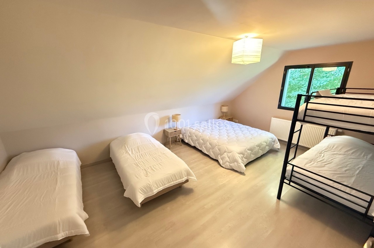 Chambre spacieuse avec trois lits simples, un lit double et un lit superposé, éclairée par une grande fenêtre.