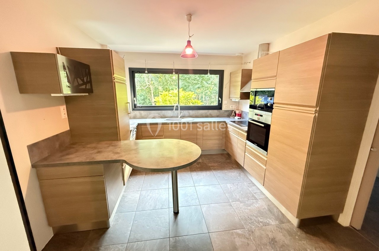 Cuisine moderne avec meubles en bois clair, plan de travail en pierre, électroménagers intégrés et grande fenêtre donnant…