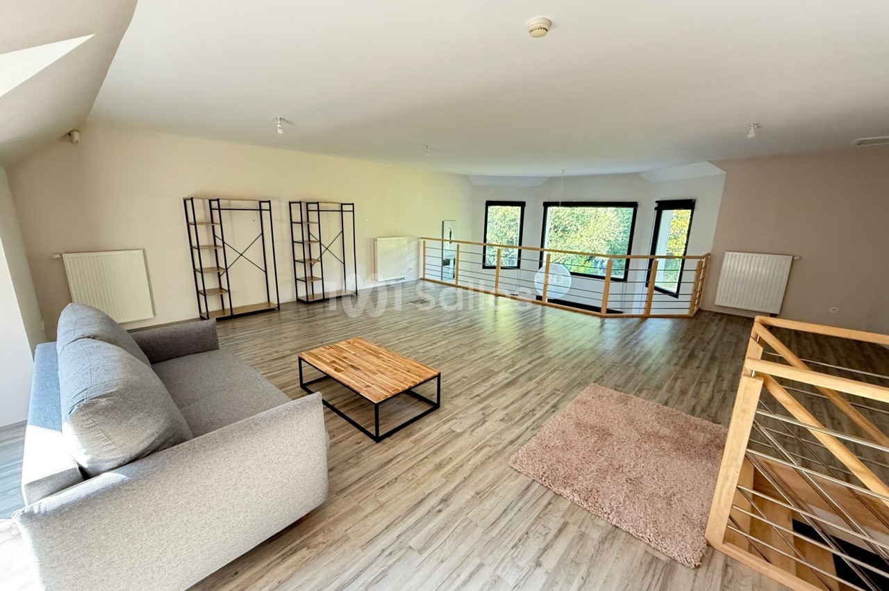Salon spacieux avec parquet clair, canapé gris, table basse en bois et grandes fenêtres donnant sur un espace vert.