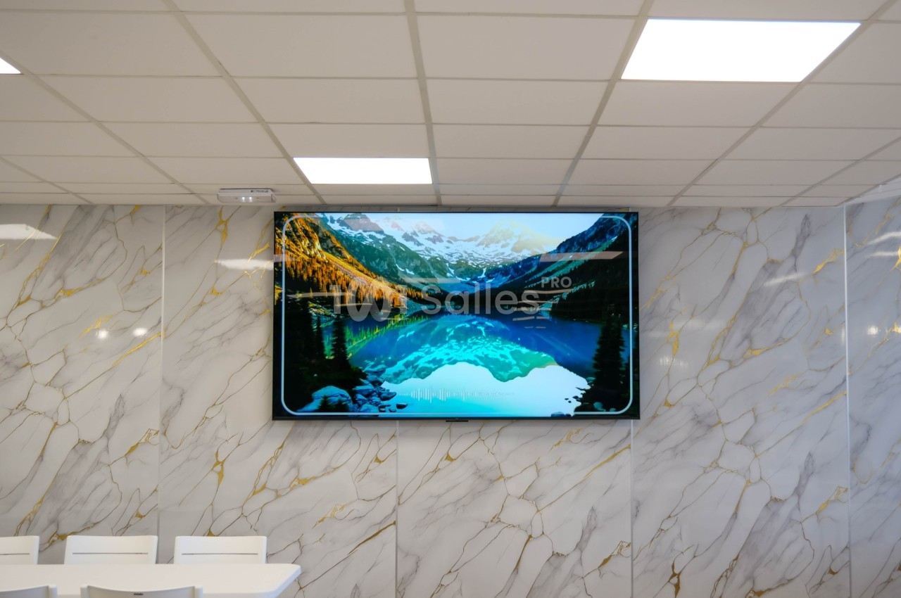 Écran mural affichant un paysage de montagne avec un lac, dans une salle aux murs en marbre et tables blanches.