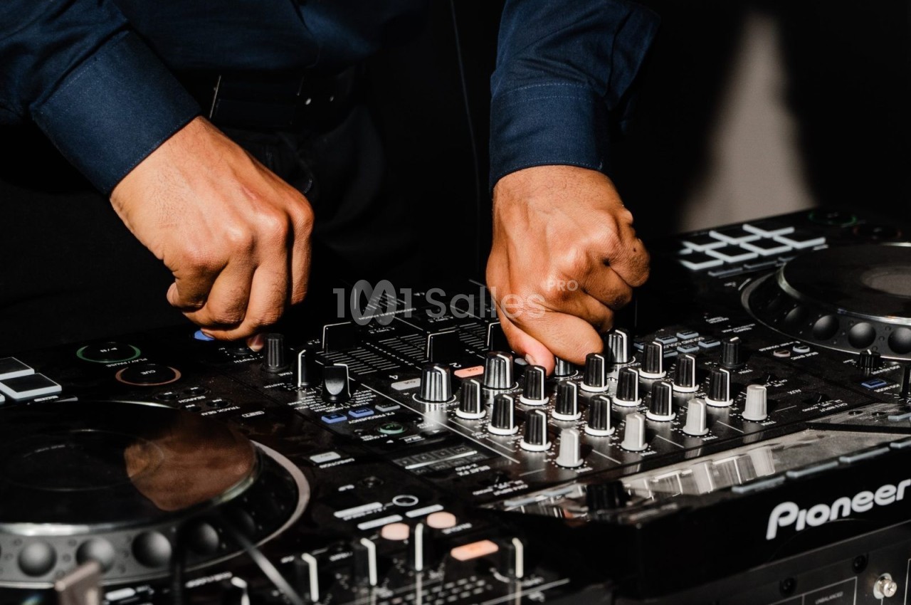 Mains ajustant les commandes d'une table de mixage audio dans un environnement sombre.