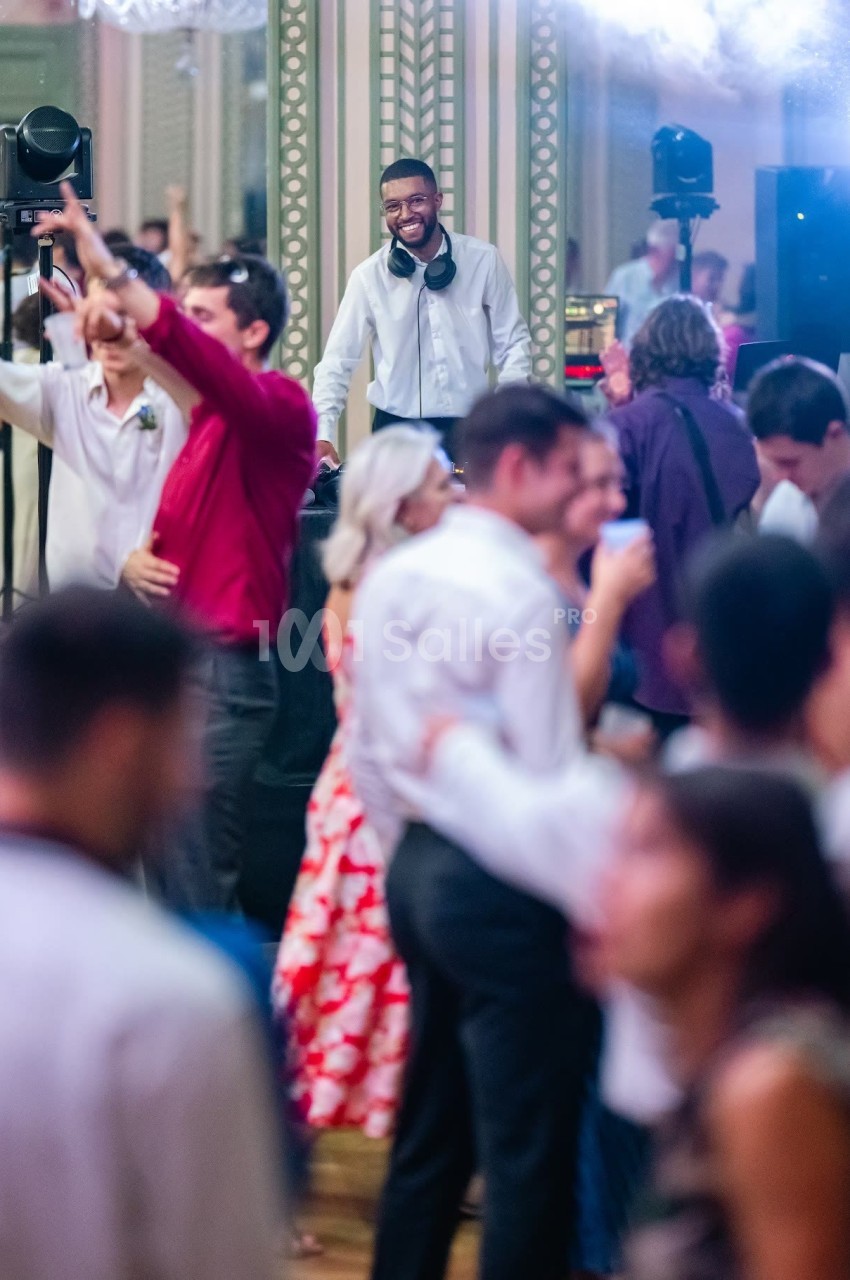 Un DJ souriant anime une piste de danse bondée lors d'une soirée festive dans une salle élégante.