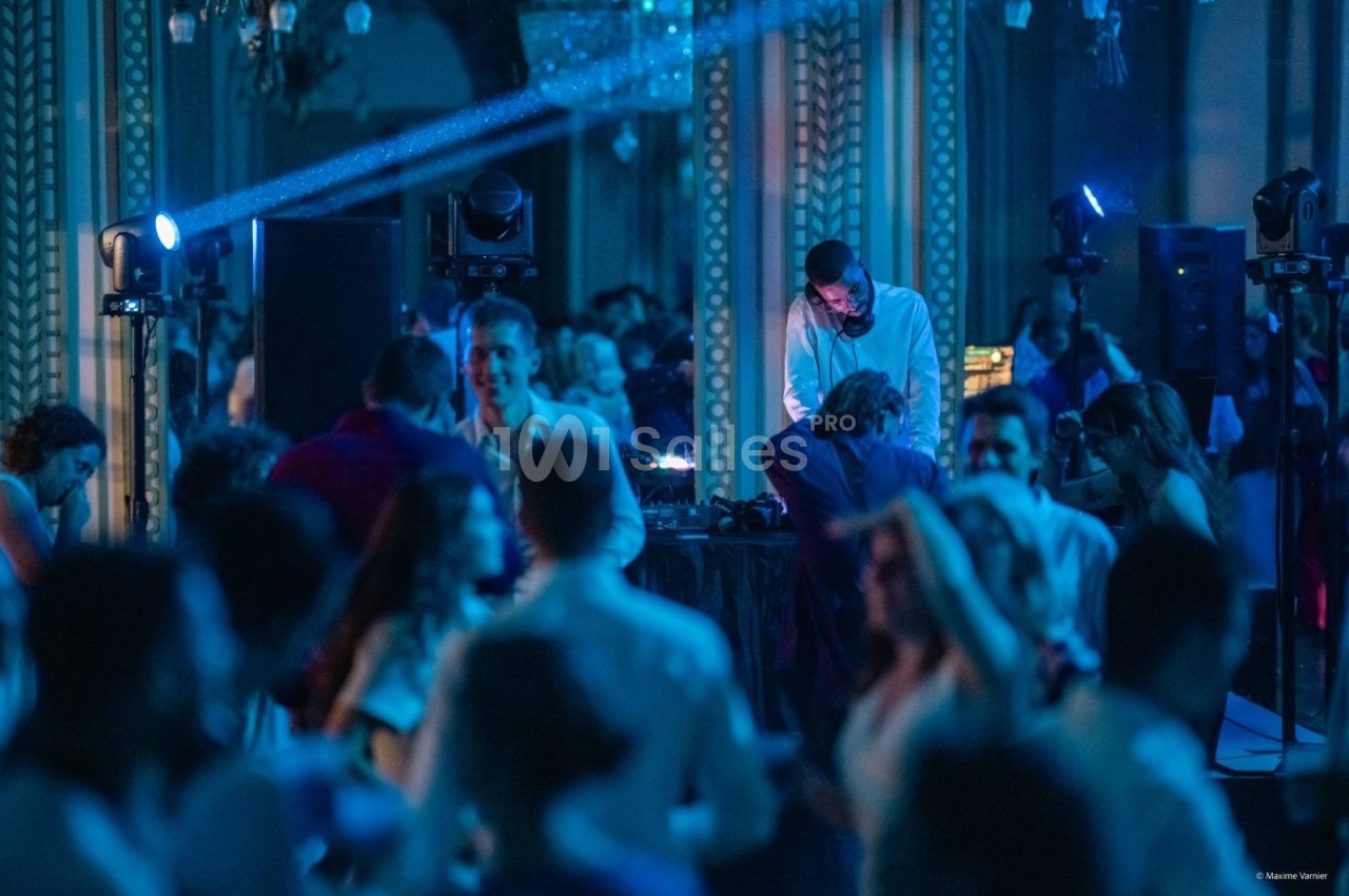 Un DJ mixe de la musique lors d'une soirée dansante, entouré de participants sous des lumières bleutées.