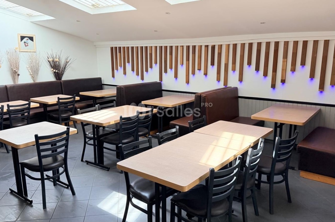 Salle de restaurant lumineuse avec tables en bois clair, chaises noires et banquettes contre un mur décoré de bois et…
