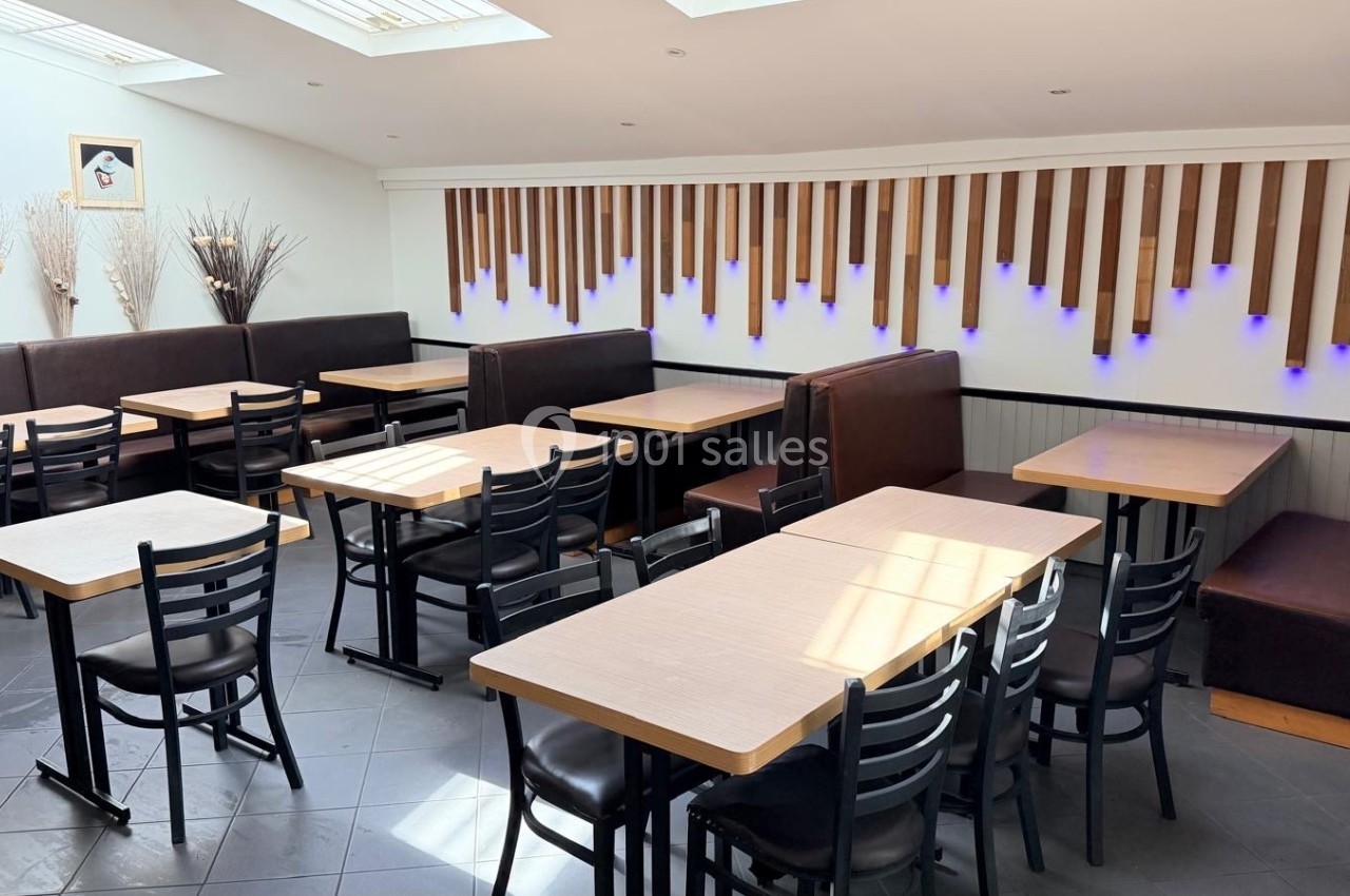 Salle de restaurant lumineuse avec tables en bois clair, chaises noires et banquettes marron, décor mural en bois et…
