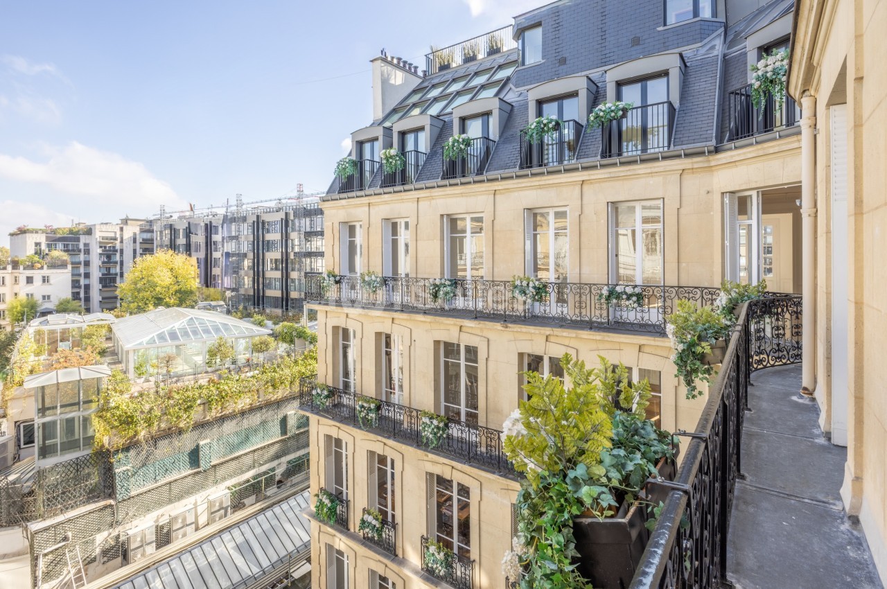 Façade d'un immeuble haussmannien avec balcons fleuris, vue sur une cour intérieure et des bâtiments modernes adjacents.