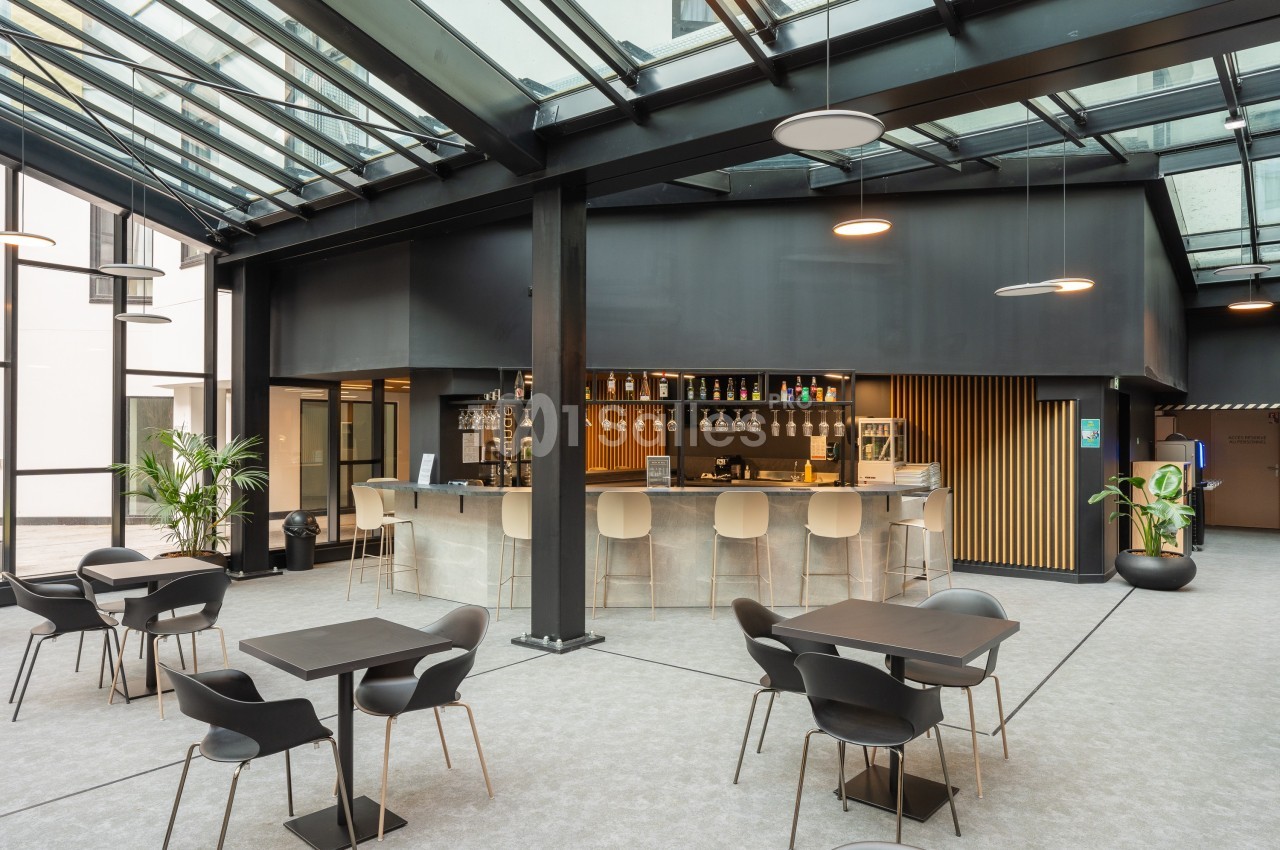 Espace intérieur moderne avec un bar central, des tables et des chaises sous une verrière.