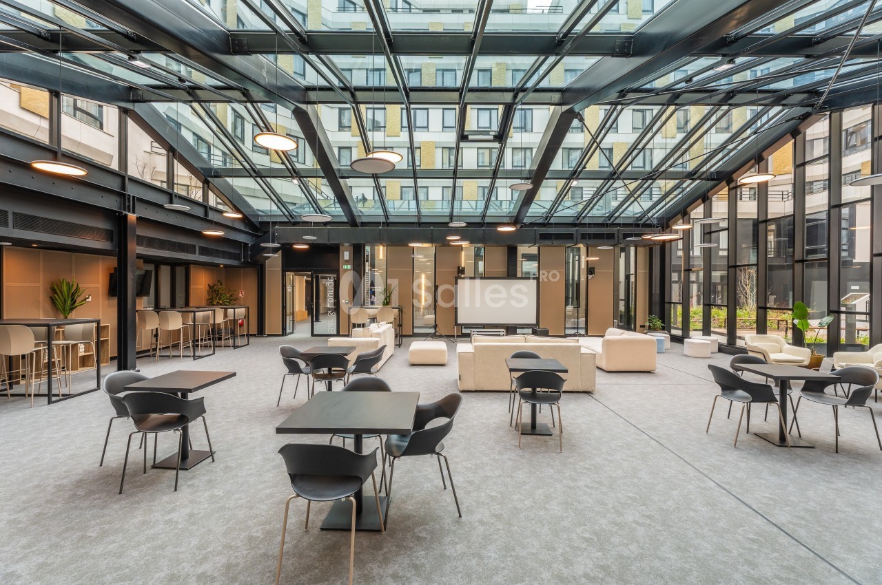 Espace intérieur lumineux avec toit en verre, mobilier moderne, tables et chaises disposées dans un cadre ouvert.