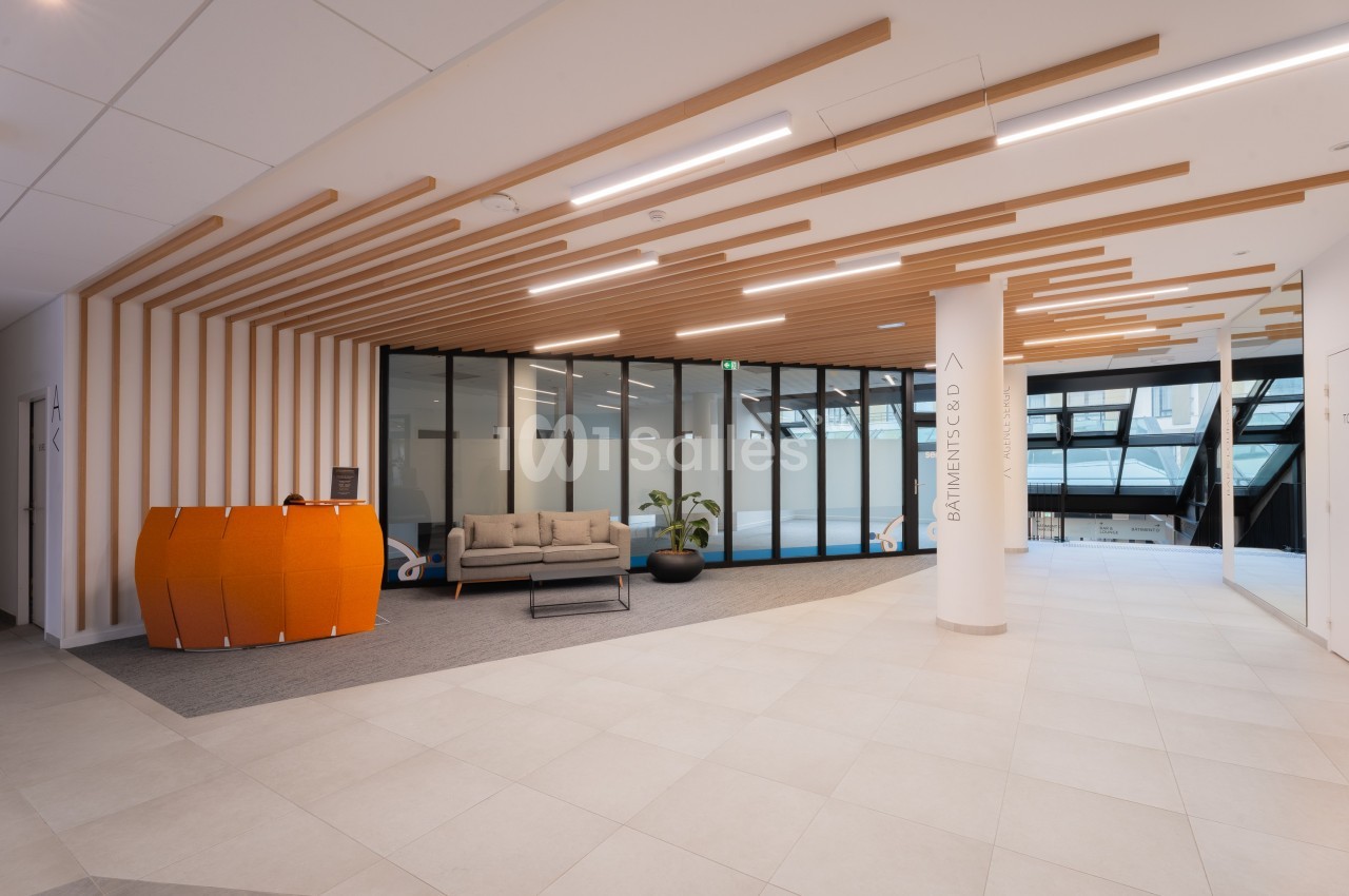 Espace d'accueil moderne avec canapé, comptoir orange et plafond en bois, séparé par des cloisons vitrées.