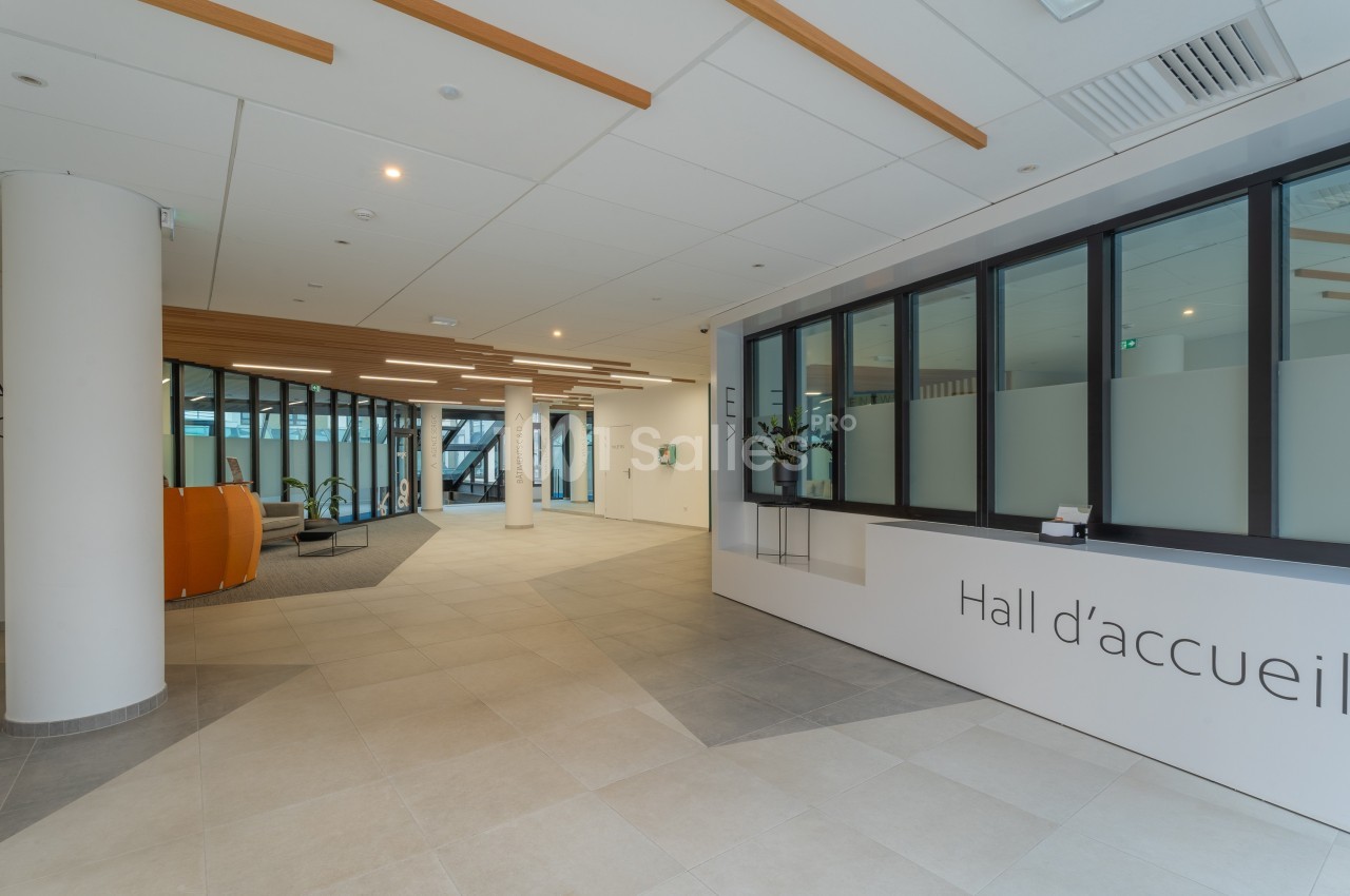 Hall d'accueil moderne avec comptoir, baies vitrées et espace d'attente aménagé dans un bâtiment lumineux.