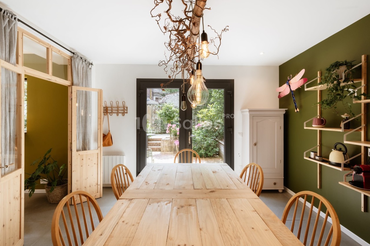 Salle à manger lumineuse avec table en bois, chaises assorties, étagères murales et vue sur un jardin verdoyant.