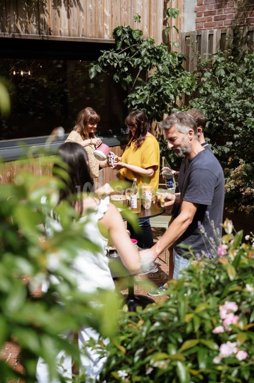 Des personnes discutent et préparent des boissons autour d'une table dans un jardin verdoyant.