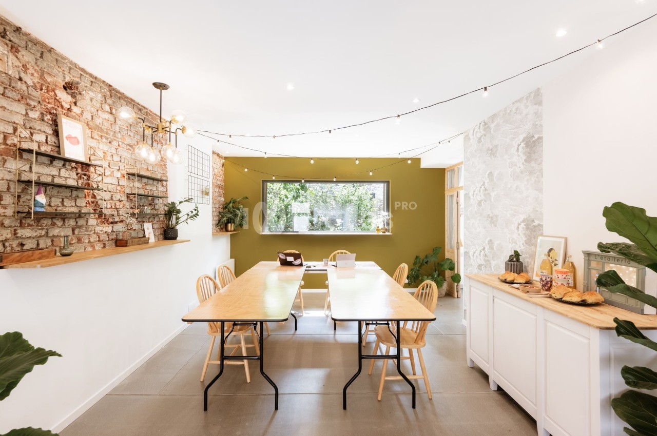 Salle à manger lumineuse avec murs en briques et verts, grande table en bois, chaises et buffet décoré.