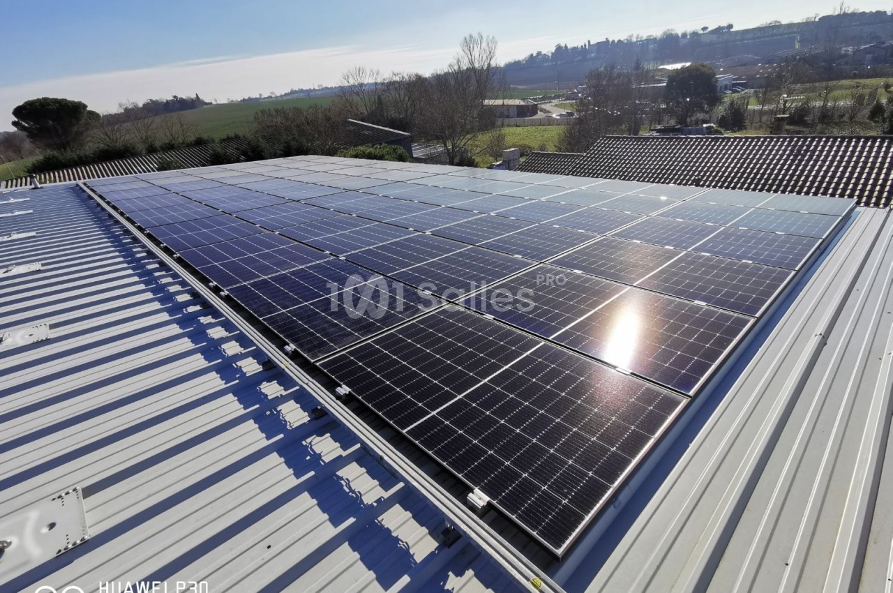 Panneaux solaires sur toit métallique ondulé, vue sur paysage rural vallonné avec champs et bâtiments.