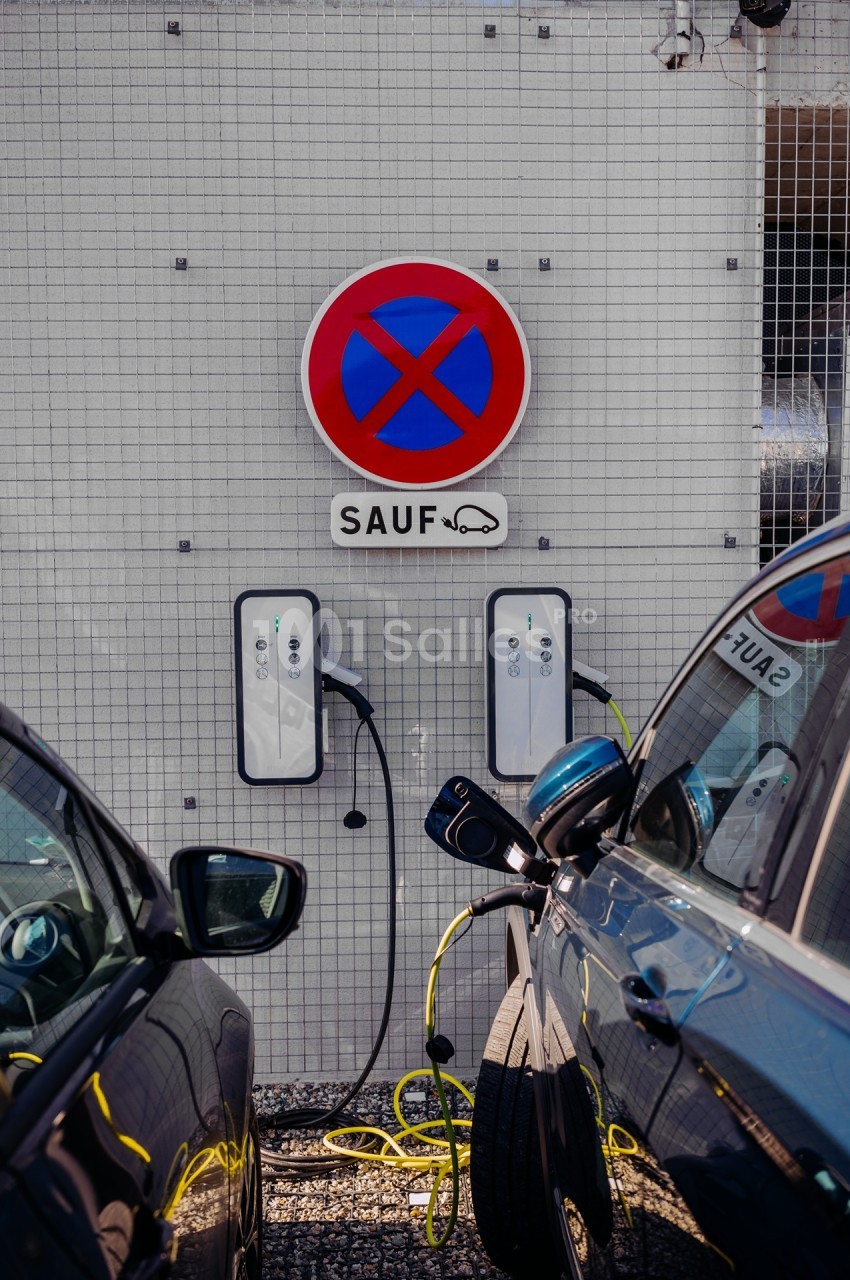 Deux véhicules électriques en charge sur deux bornes murales - panneau d'interdiction de stationner au-dessus.