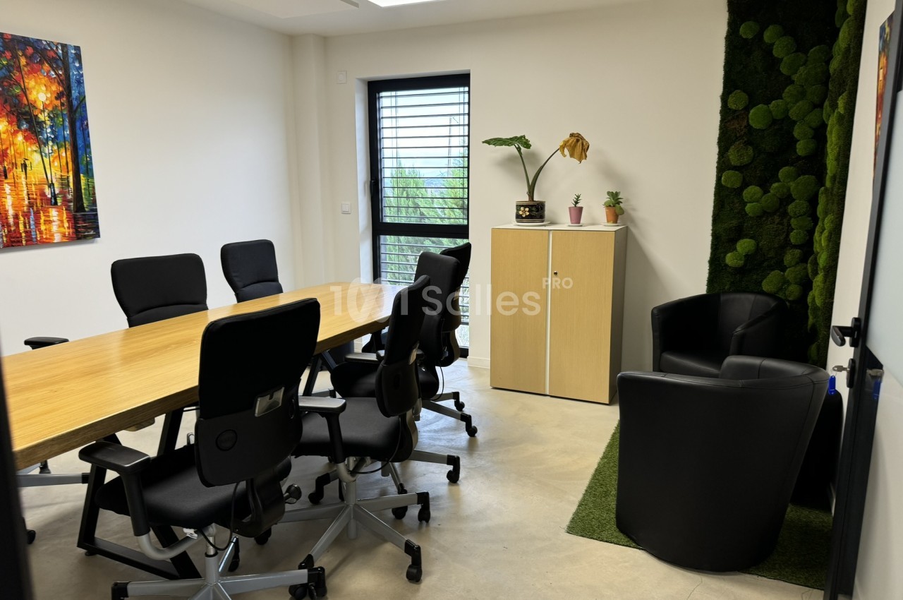 Salle de réunion moderne avec table en bois clair, chaises noires, mur végétal, et baie vitrée sur jardin.