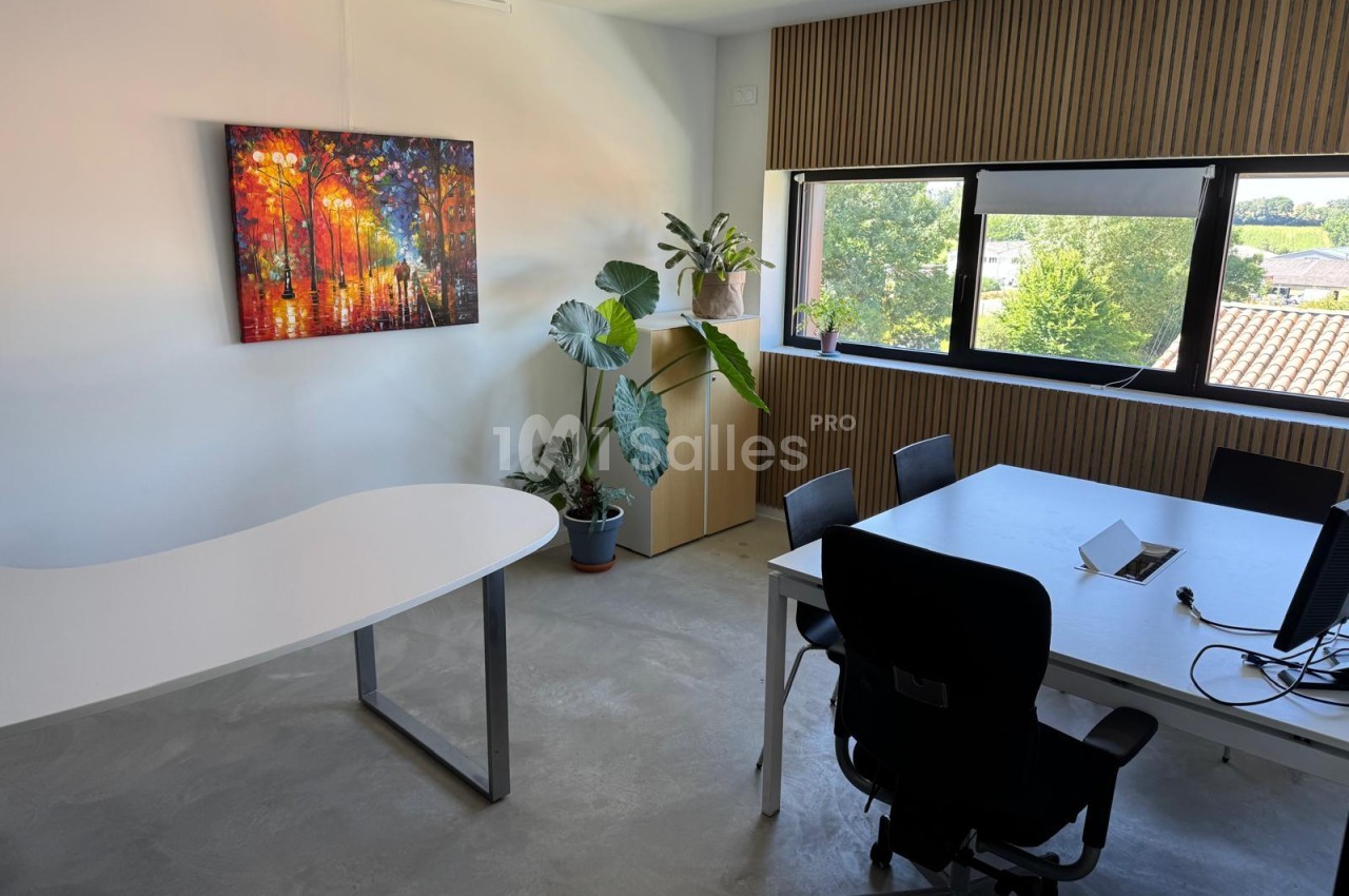 Salle de réunion avec deux tables blanches, chaises noires, baies vitrées donnant sur la campagne et décoration végétale.