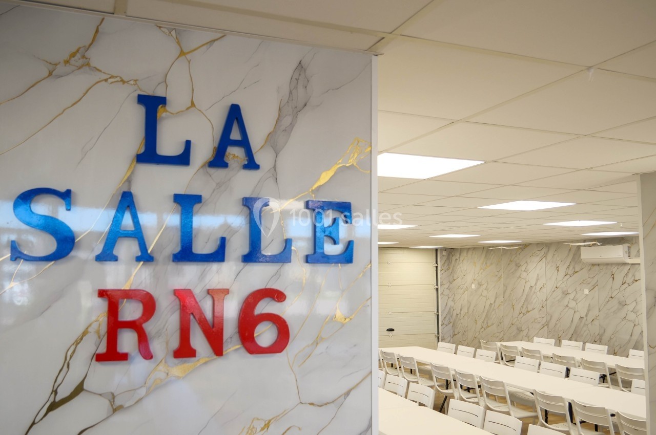Salle de réunion lumineuse avec murs en marbre clair, tables blanches et inscription ’La Salle RN6’ en avant-plan.