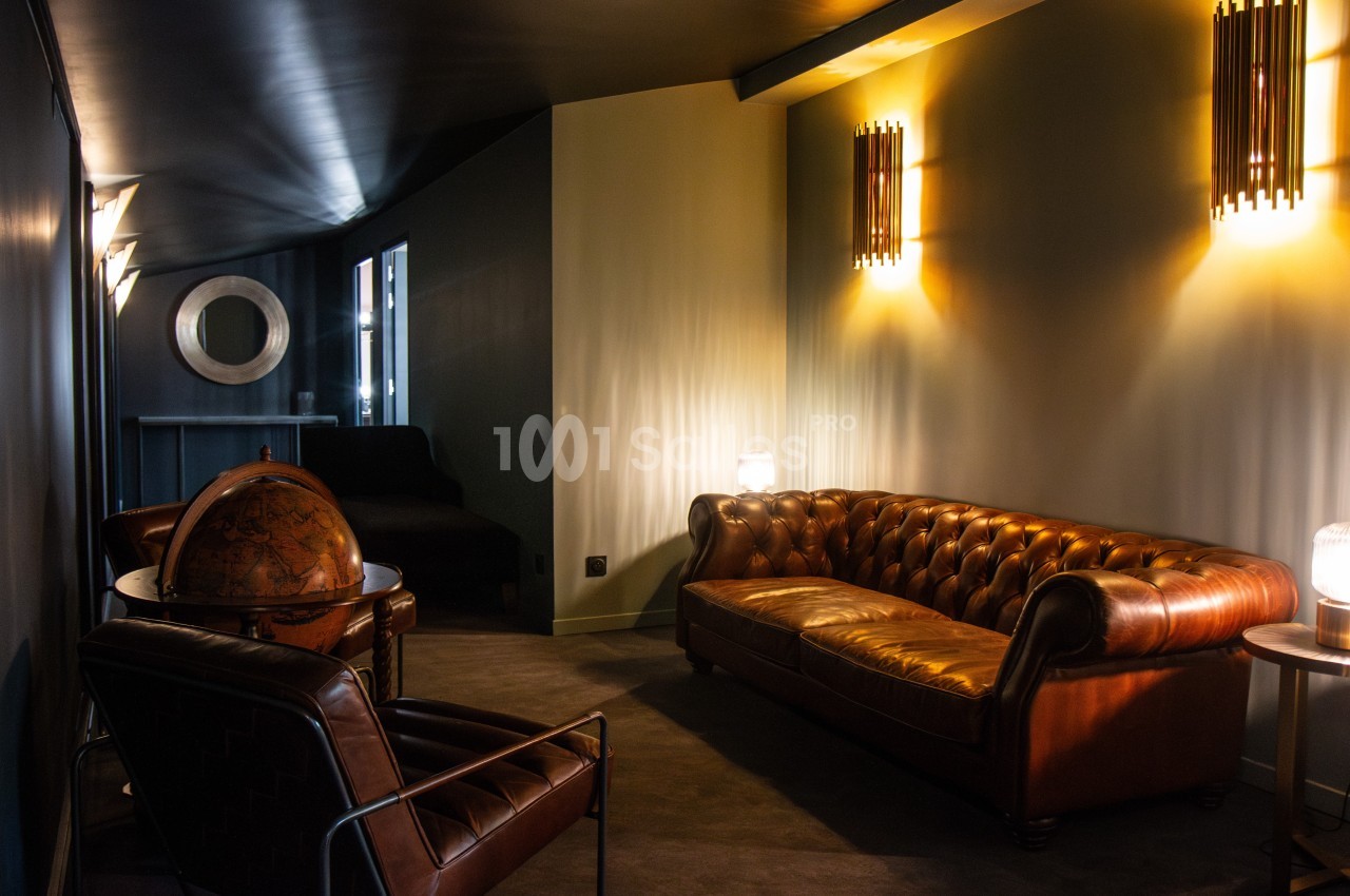 Salon cosy avec canapé en cuir marron, fauteuils assortis, globe terrestre et éclairage tamisé.
