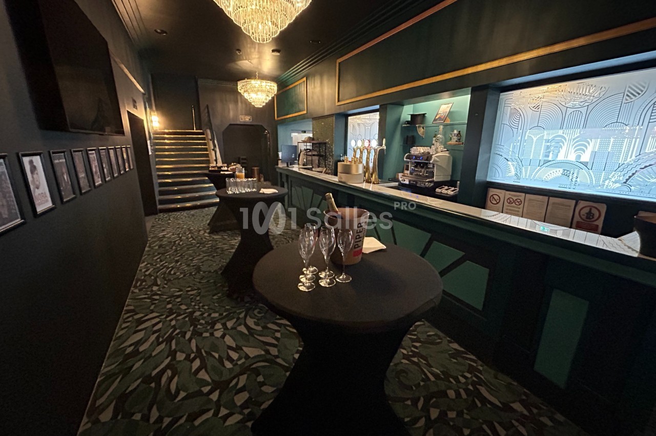 Salle élégante avec bar, tables hautes noires, seaux à champagne et lustres suspendus dans une ambiance tamisée.