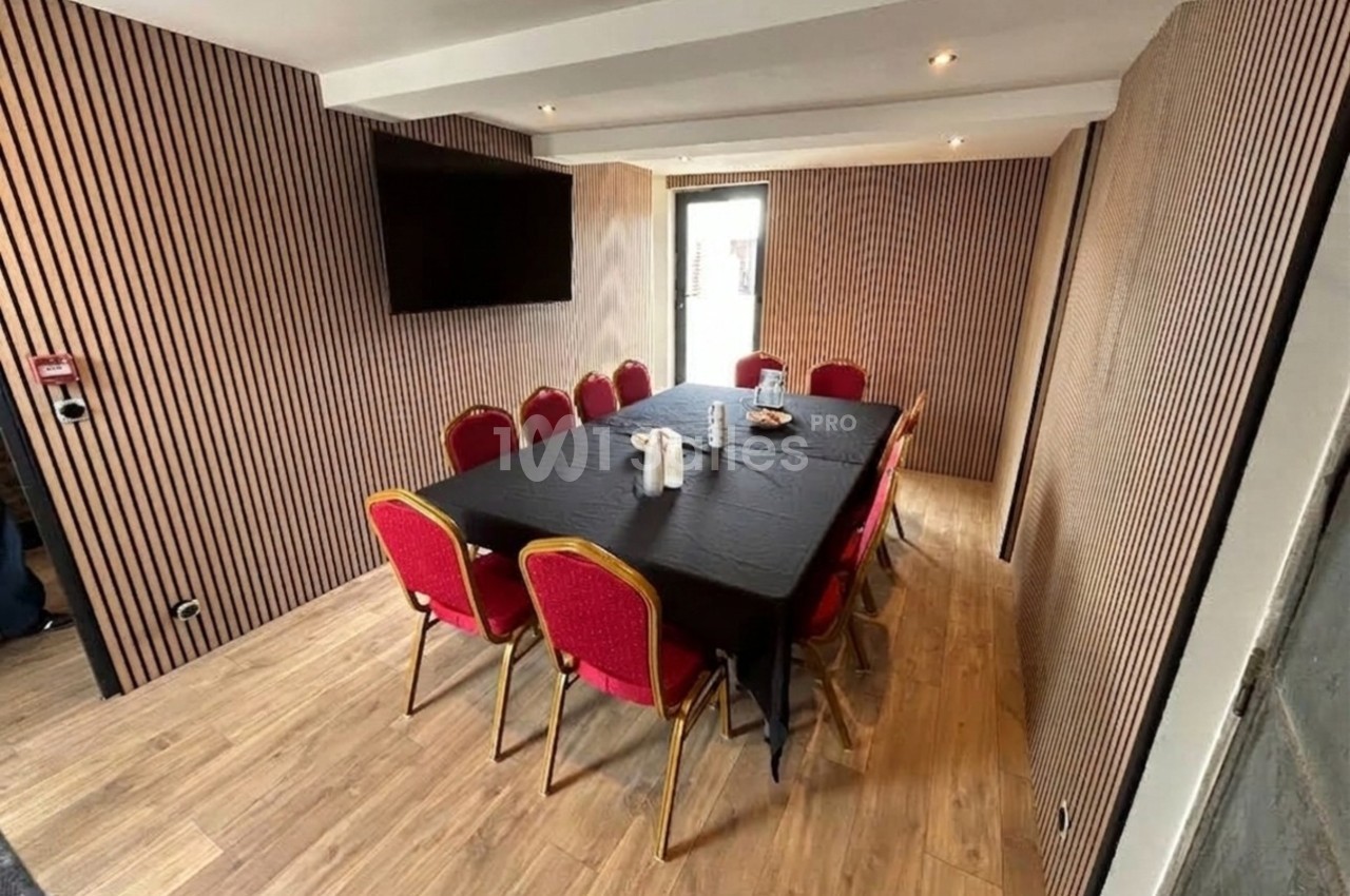 Salle de réunion avec table rectangulaire noire, chaises rouges, murs en bois strié et écran mural.