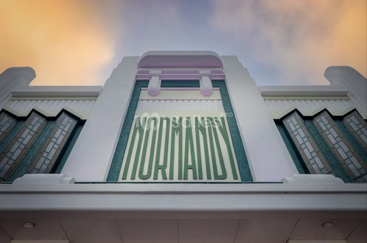 Façade art déco d'un bâtiment avec l'inscription ’Normandy’ en lettres vertes sur fond pastel.