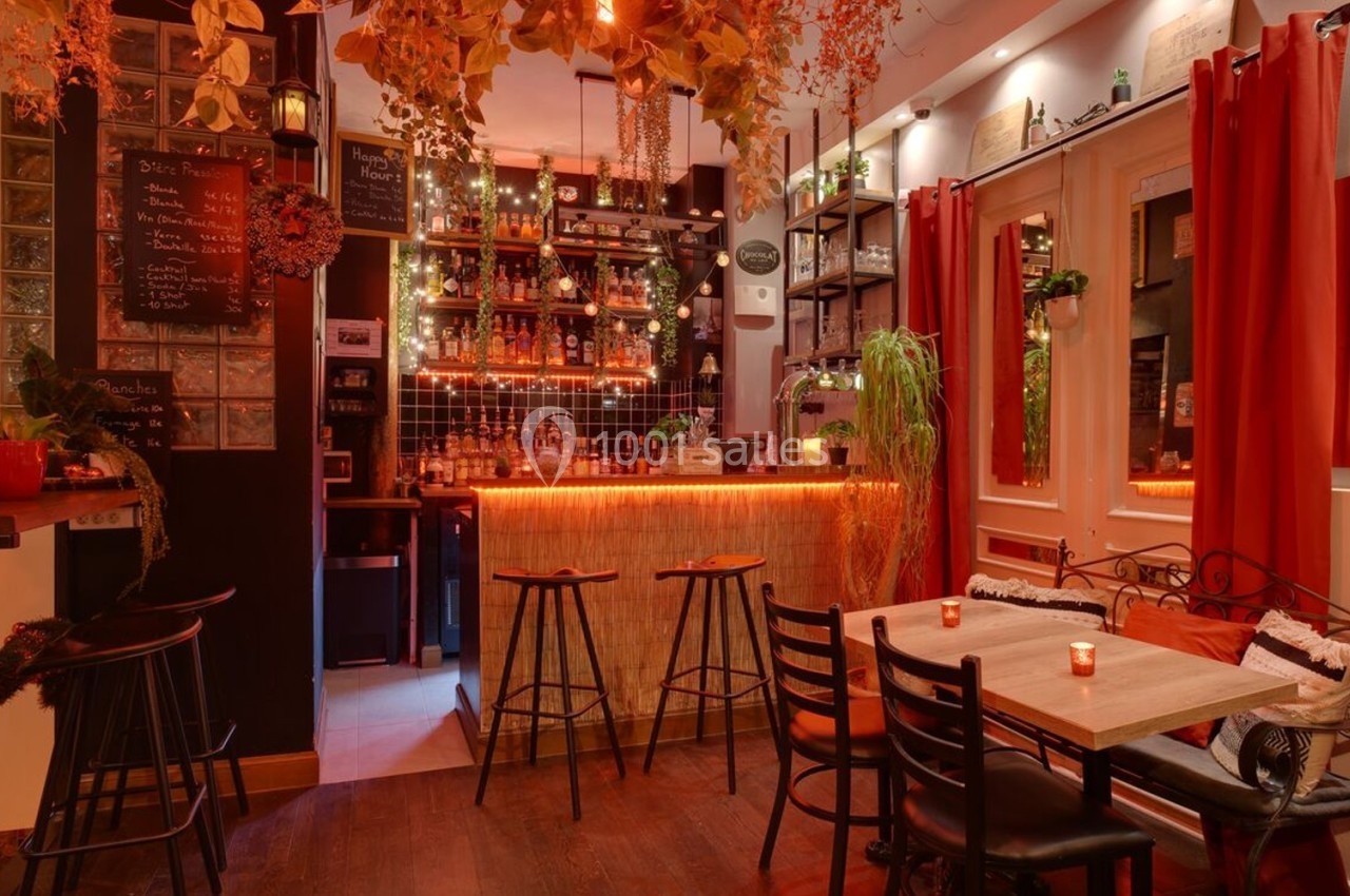 Intérieur d'un bar chaleureux avec éclairage tamisé, comptoir en bois, tabourets hauts et décorations végétales.