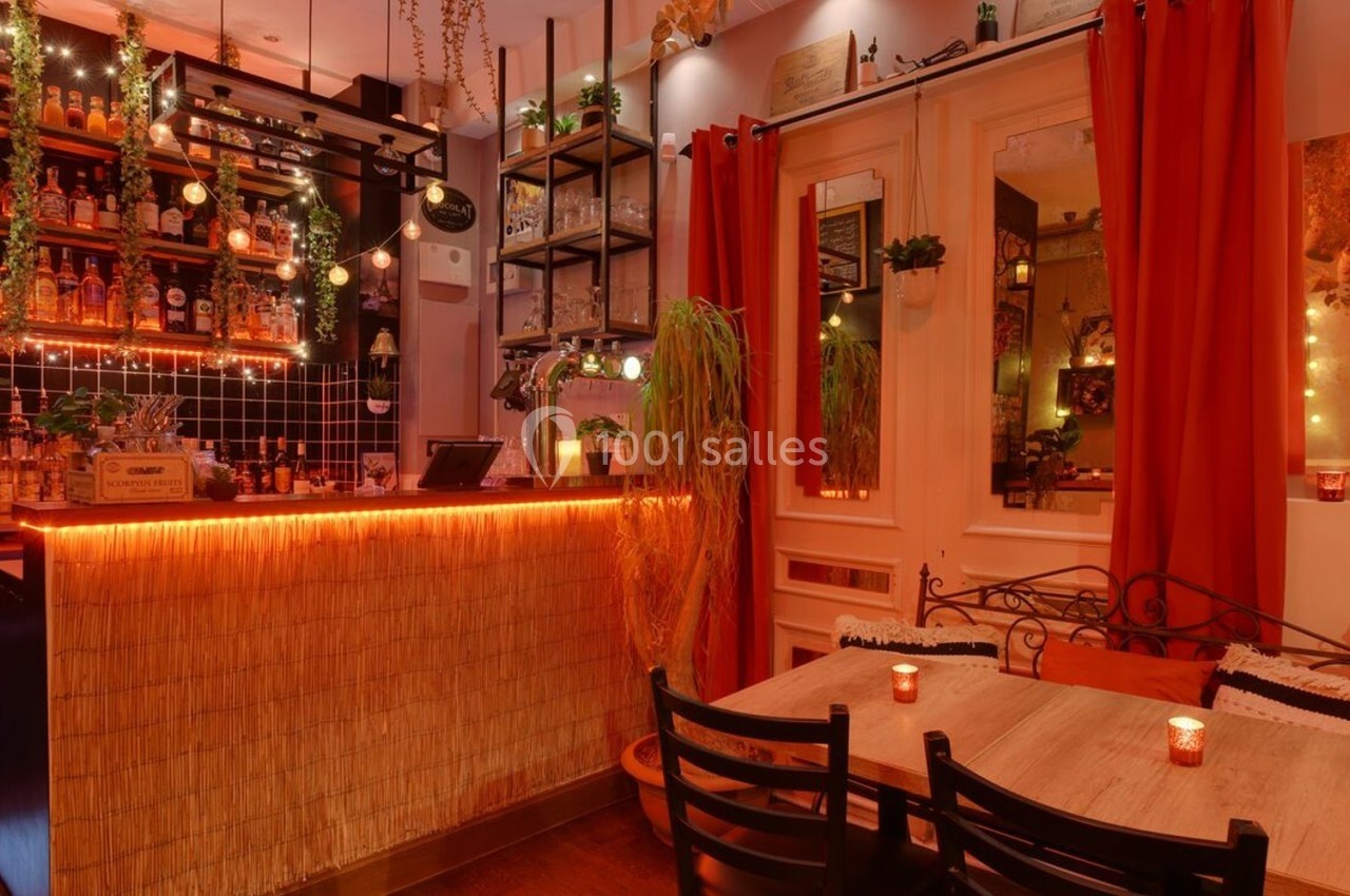 Intérieur d'un bar chaleureux avec un comptoir éclairé, étagères de bouteilles, tables en bois et décorations lumineuses.