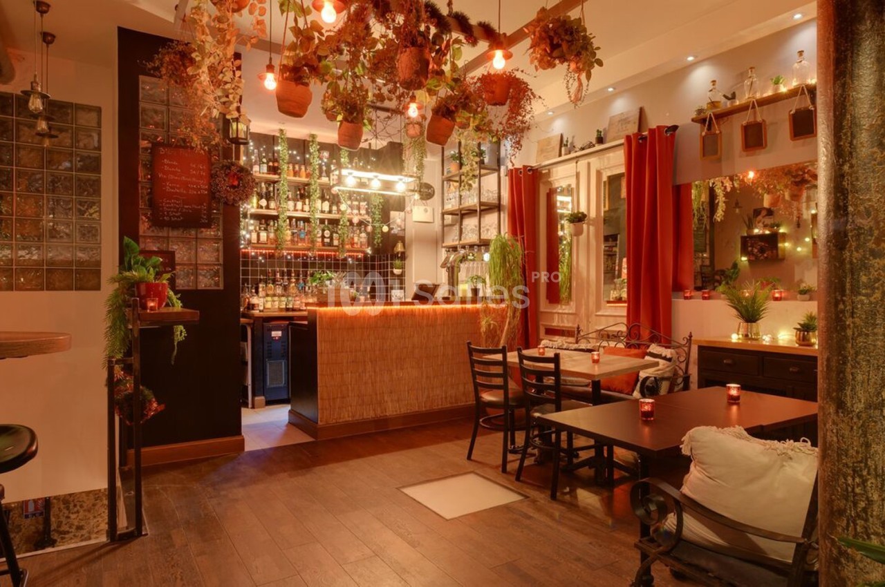 Salle de restaurant chaleureuse avec décoration végétale suspendue, éclairage tamisé et mobilier en bois.