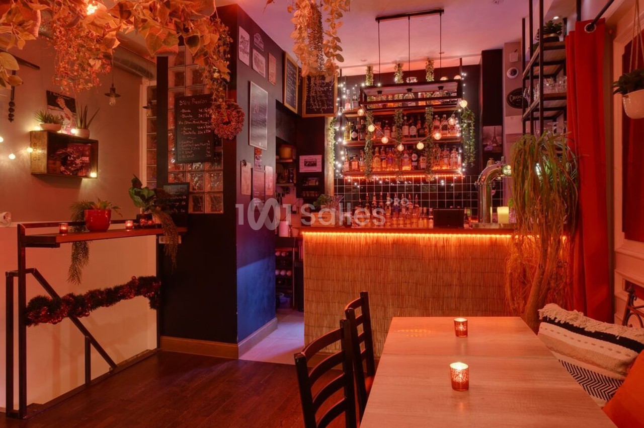 Intérieur d'un bar chaleureux avec éclairage tamisé, décor végétal et comptoir illuminé.