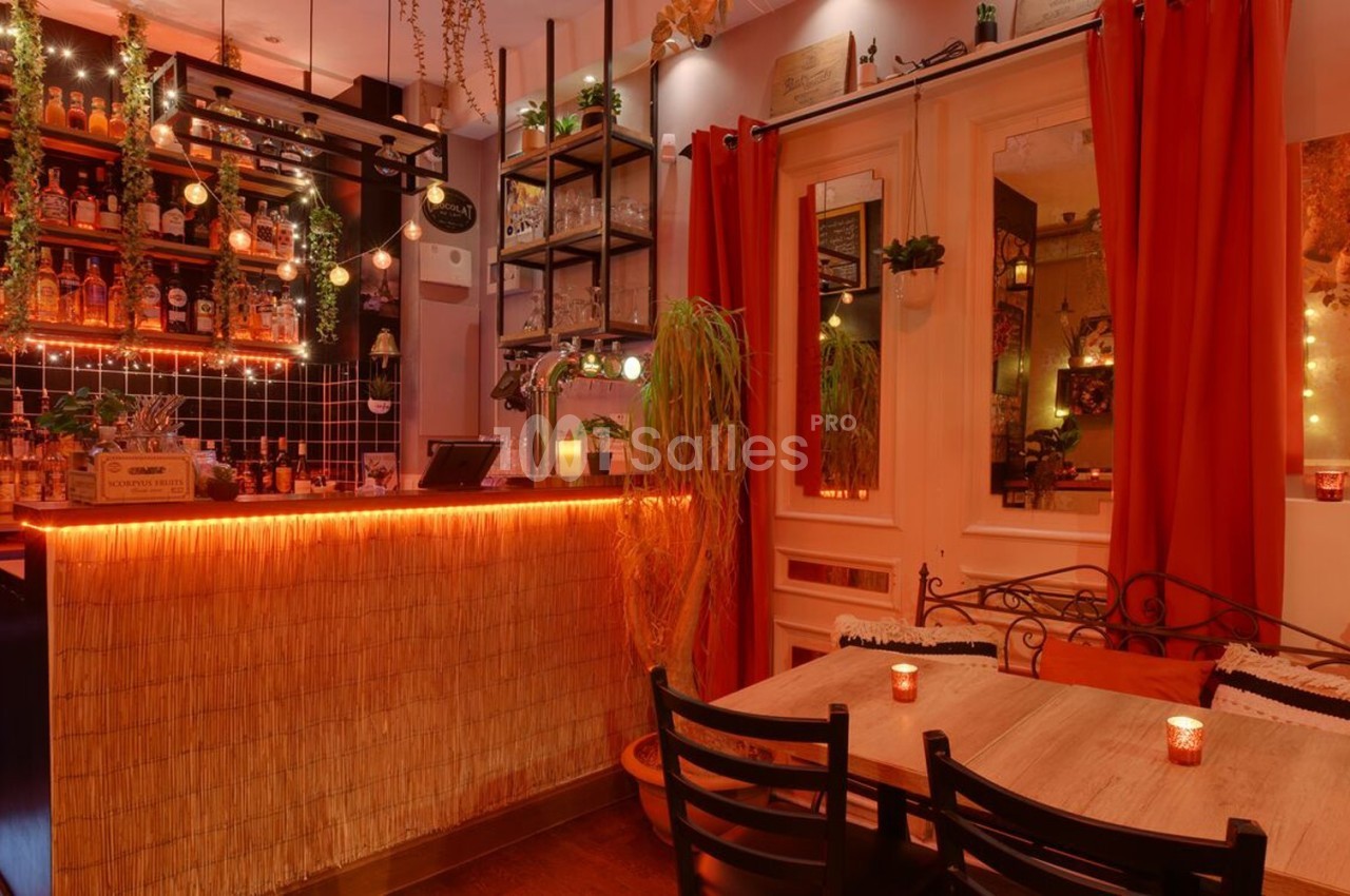 Intérieur d'un bar chaleureux avec un comptoir éclairé, des étagères de bouteilles et des tables en bois décorées de bougies.