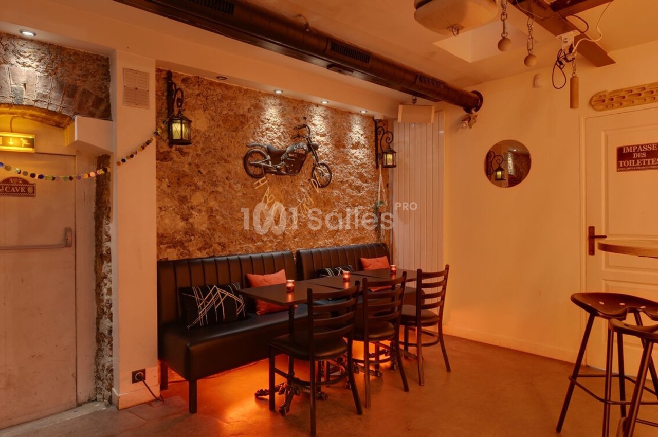 Salle chaleureuse avec murs en pierre, banquette, table et chaises en bois, éclairage tamisé et décoration murale.