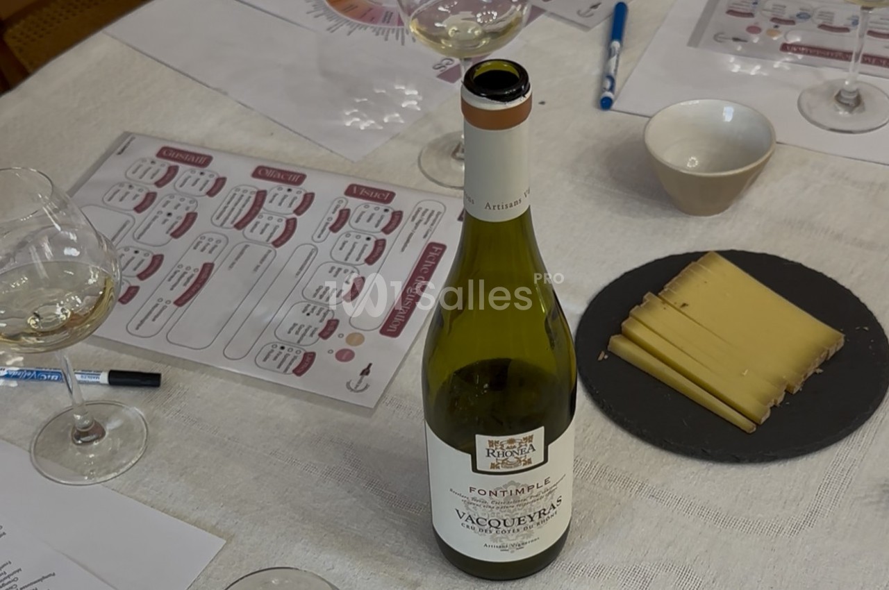 Bouteille de vin blanc, verres, assiette de fromage et documents sur une table lors d'une dégustation.