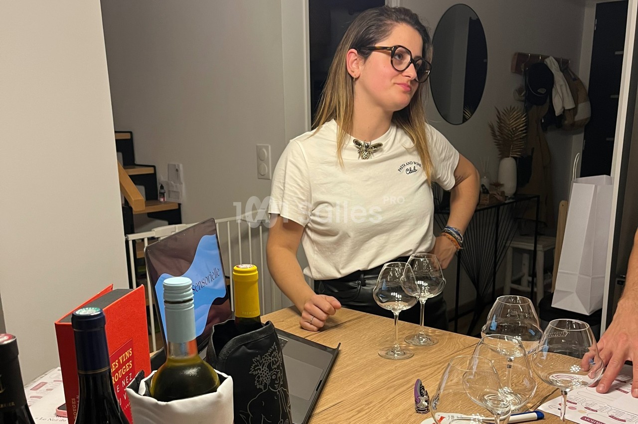 Une femme debout près d'une table avec des verres à vin, dans un intérieur moderne et éclairé.